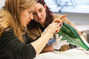 Zwei Studentinnen beim Inventarisieren einer Glasflasche